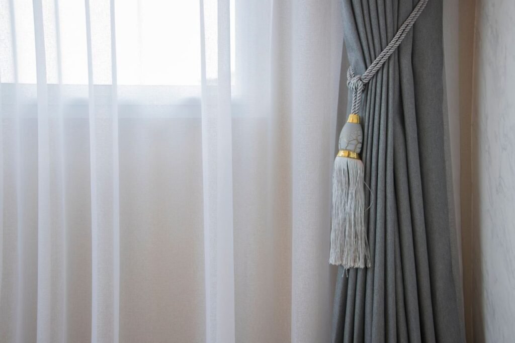Soft gray curtain with decorative tieback in a bright room, adding elegance to home decor.