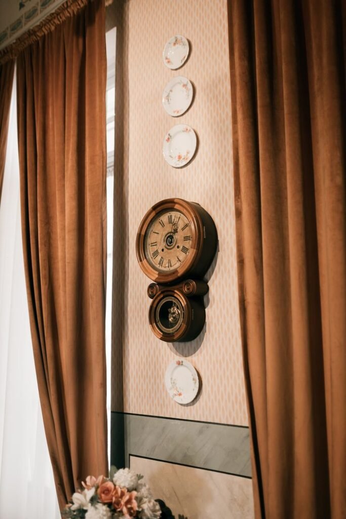 Vintage wall clock and floral plates on a stylish interior wall with curtains.