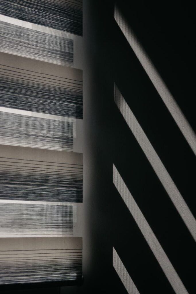 Modern window blinds create striking shadows on a wall for an abstract visual effect.